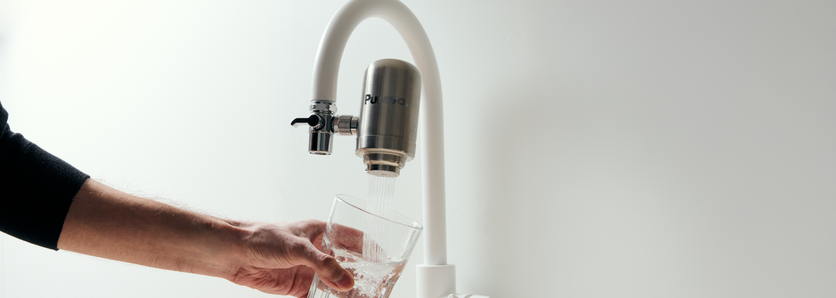 Filtre à eau Pureva One monté sur un robinet, eau filtrée coulant dans un verre